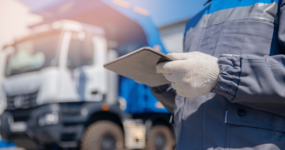 A waste collections professional takes notes on a tablet while standing in front of a clean, well-maintained garbage truck.